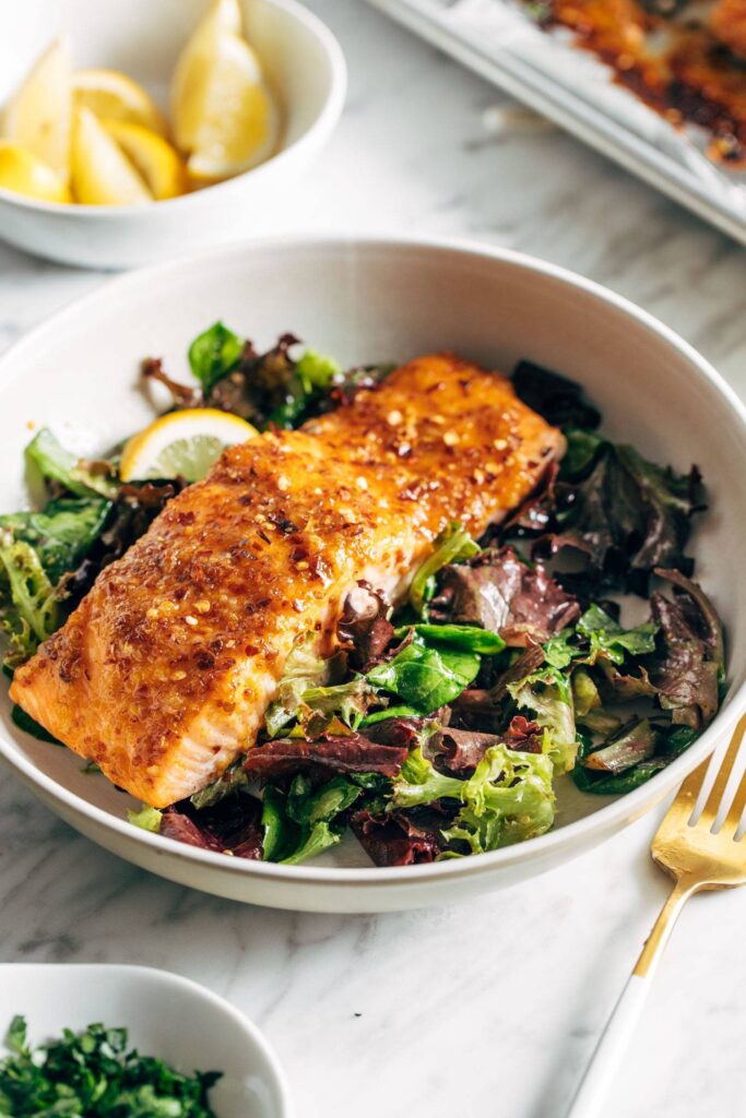 Hot honey salmon in a bowl on top of a green salad. There