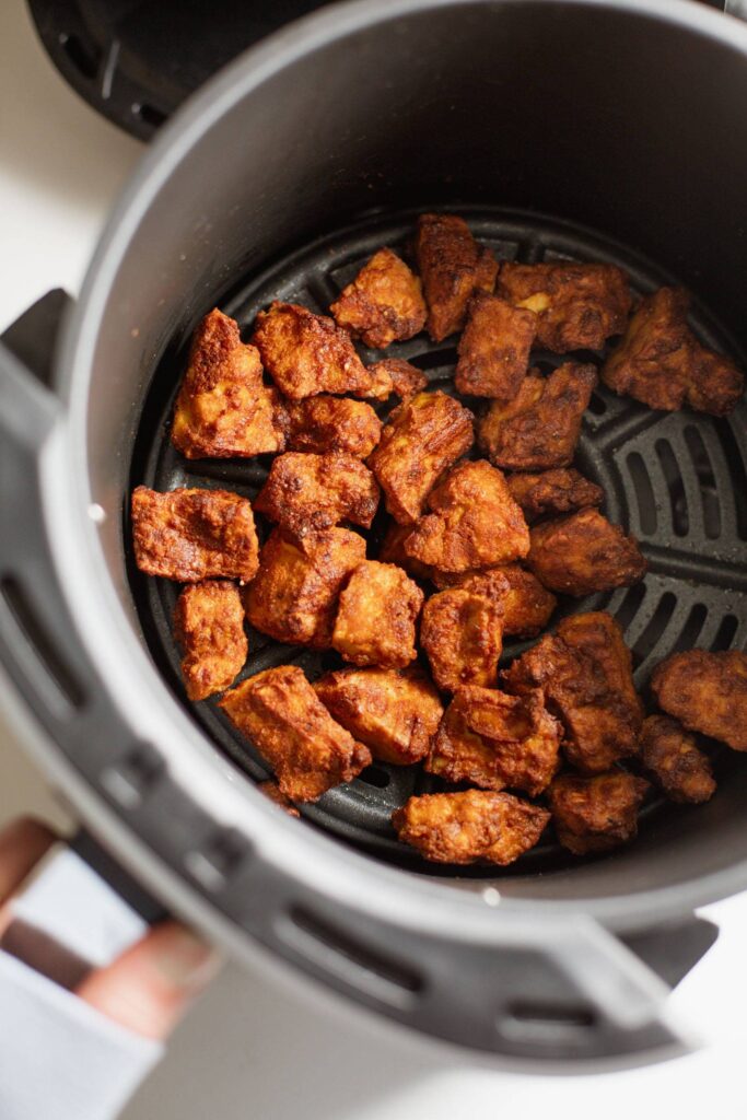 Seasoned tofu in the basket of an air fryer.