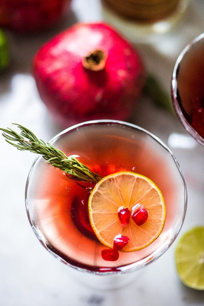 Festive Pomegranate Martini with a sprig of rosemary, lime and pomegranate seeds.