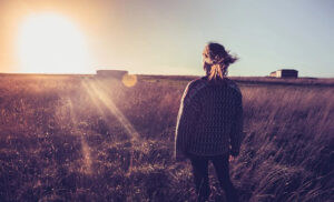 Woman looking at the sunset while standing in a late summer field.