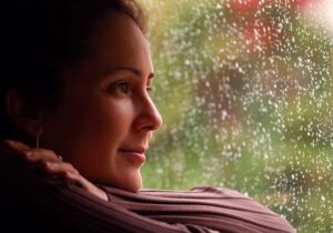 Woman looking out of rainy window with a slight smile on her face.