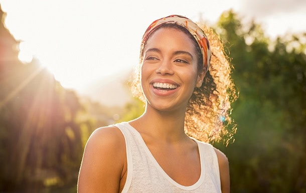 10 Simple Ways to Spread the Optimism and Positive Energy Starting Today A smiling woman outside in the sunshine.