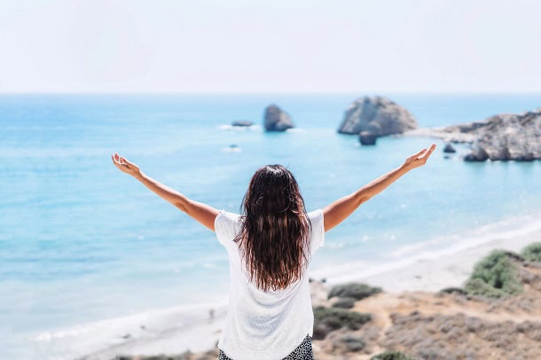 The Top 10 Ways to Be Kind to Yourself Starting Today A woman raising her hand while watching the view at the ocean.