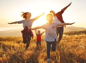 A happy family running towards the camera in a field of grass with their arms stretched out imitating airplanes.
